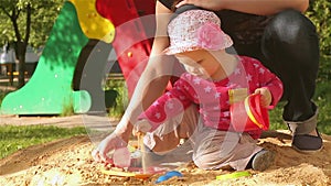 A little girl is playing with her mother in the sandbox.