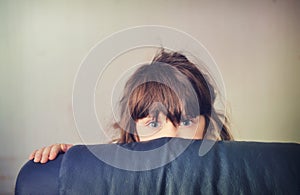 Little girl playing hide and seek behind the sofa