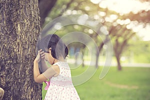 little girl is playing hide-and-seek hiding face in the park.