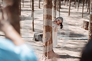 Little girl playing hiding behind tree and waving hand with family