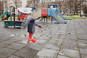 Little girl playing and jumping in rain puddle on an empty kids playground during a winter day in Bucharest, Romania