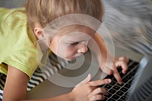 A little girl is playing on the laptop at home. Child, playing, home
