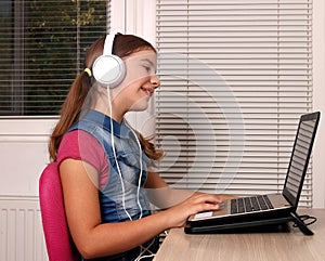 Little girl playing laptop and listening music on headphon