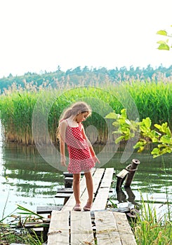Little girl is playing and looking at the lake at summer day