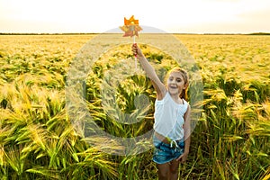 Little girl playing on the meadow on sun with windmill on wheat field