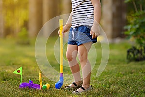 Little girl playing mini golf in spring park. Child having fun with active leisure on vacations