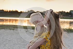 Little girl playing with moms hair. Portrait in motion mother and child on river and sunset background