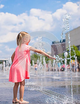 Little girl playing in open street fountain at hot