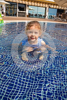 Little girl playing in outdoor swimming pool, jumping into water on summer vacation . Child learning to swim in outdoor