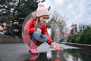 Little girl playing with paper boat near puddle outdoors