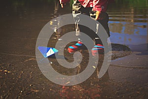 Little girl playing with paper boats in puddle