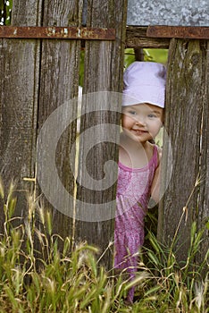 Little girl playing peek a boo through a gap in a broken plank