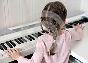 A little girl playing the piano: look from the back