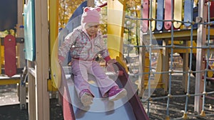 Little girl playing on the playground in the autumn afternoon. The child goes down the hill