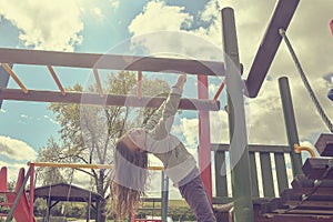 Little girl playing on playground, hanging walk along the monkey bars.