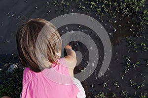 Little girl playing in puddle at summer. Black dirt puddle after rain. Exploring surroundings world