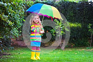 Little girl playing in the rain under colorful umbrella