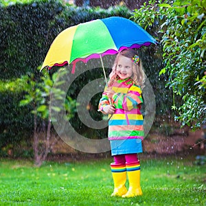 Little girl playing in the rain under colorful umbrella