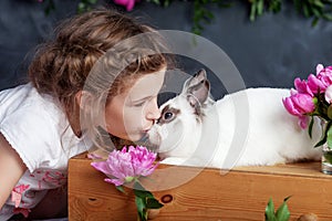 Little girl playing with real rabbit. Child and white bunny on Easter on flower background. Kid kiss pet. Fun and friendship for