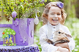 Little girl  playing with real rabbit in the garden. Laughing child at Easter egg hunt with  pet bunny. Spring outdoor fun for