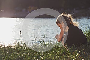 Little girl is playing on the river bank in summer
