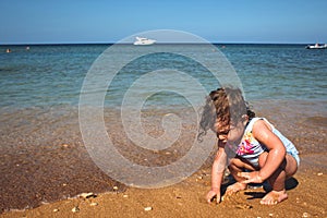 Little girl playing on a sandy beach by the sea