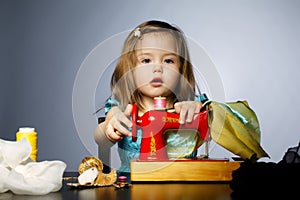 Little girl is playing with sewing machine