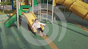 Little girl playing slide alone at the playground in the morning. The footage may contain noise due to low light
