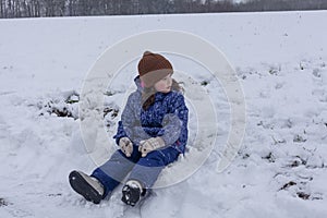 Little girl playing in the snow on a sunny winter day. She is wearing a warm hat and blue jacket