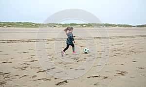 Little girl playing soccer on the beach