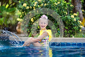 Little girl playing and spraying water in swimming pool outdoors at summer. Summer vacation concept