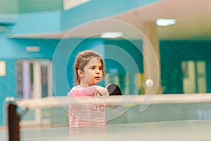 Little girl playing table tennis in the tennis hall, tennis racket hitting the ball