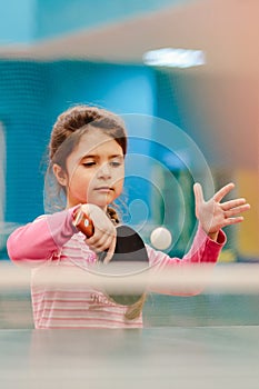 Little girl playing table tennis in the tennis hall, tennis racket hitting the ball, the pitch of the ball