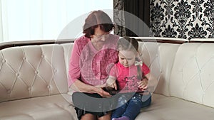 Little girl playing on tablet with grandmother.