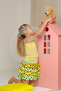 Little girl playing with a teddy bear in a toy wooden house.