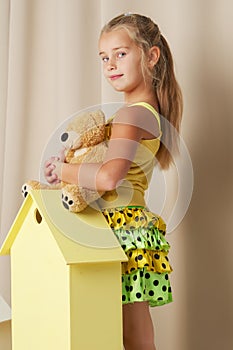 Little girl playing with a teddy bear in a toy wooden house.