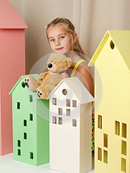 Little girl playing with a teddy bear in a toy wooden house.