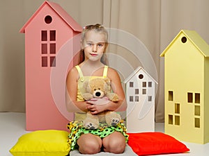 Little girl playing with a teddy bear in a toy wooden house.