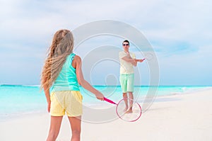 Little girl playing tennis with father on white tropical beach