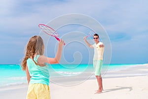 Little girl playing tennis with father on white tropical beach