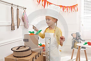 Little girl playing with toy cardboard kitchen at home