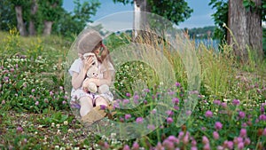 A little girl playing with a toy rabbit in the meadow among the flowering clover