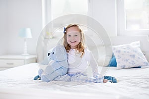 Little girl playing with toy and reading a book in bed