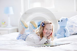 Little girl playing with toy and reading a book in bed