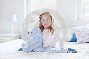 Little girl playing with toy and reading a book in bed