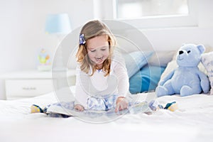 Little girl playing with toy and reading a book in bed