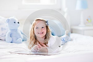 Little girl playing with toy and reading a book in bed