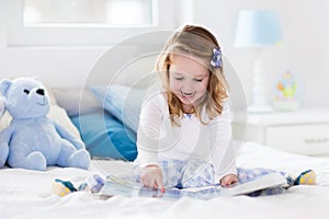 Little girl playing with toy and reading a book in bed