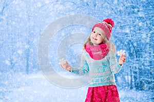 Little girl playing with toy snow flakes in winter park