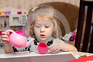 A little girl is playing with a toy tea set in the kitchen at the table